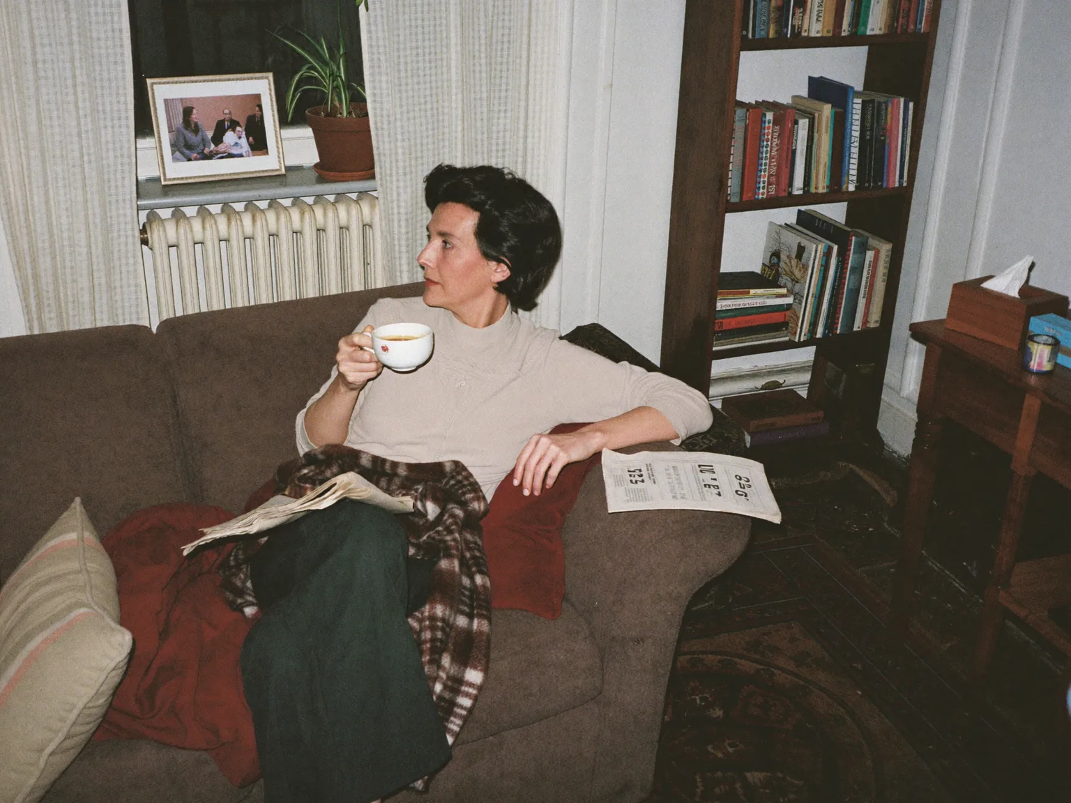 Frau sitzt mit einer Tasse Tee unter einer Decke auf dem Sofa