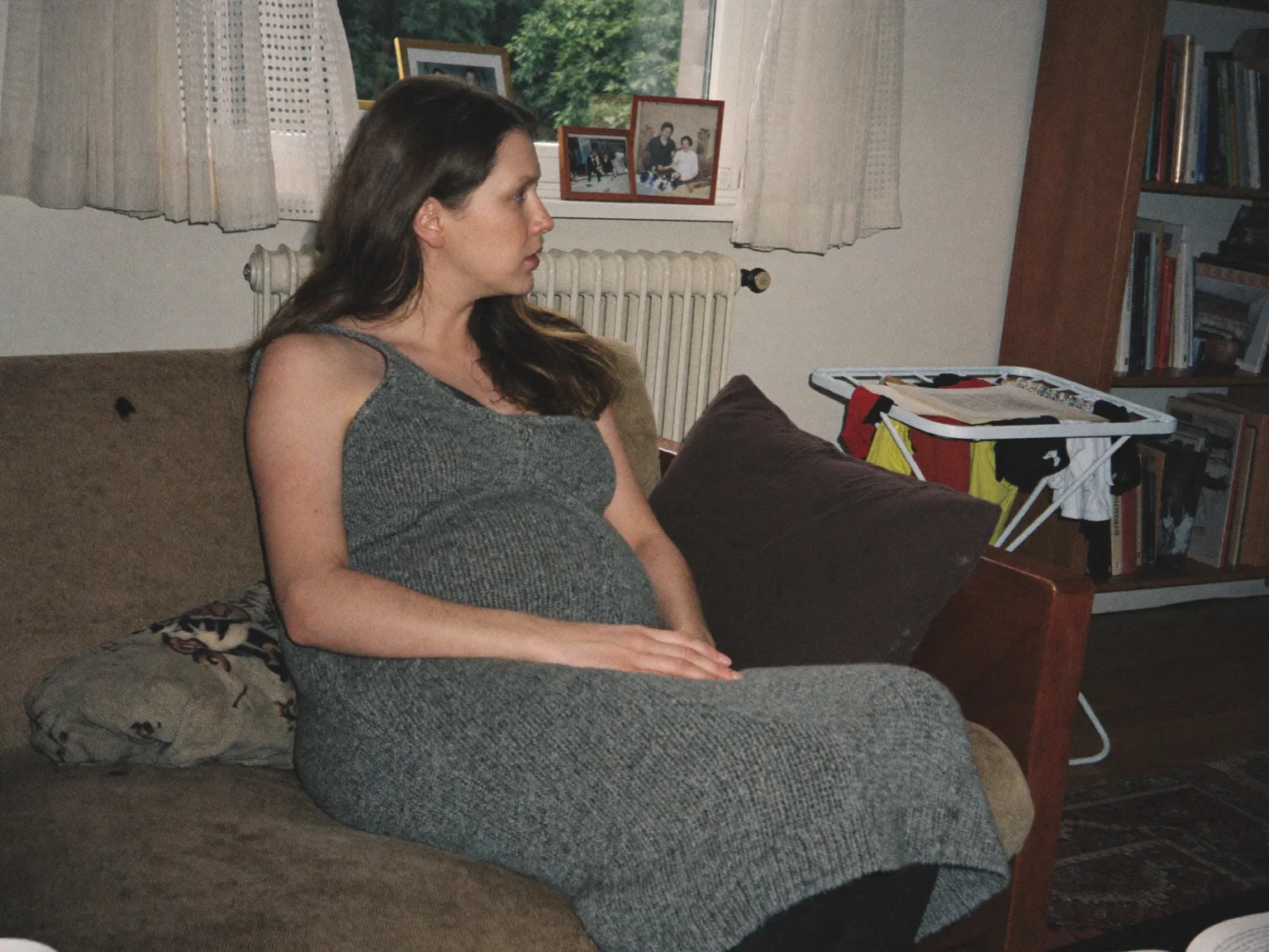 Schwangere sitzt auf dem Sofa und sieht aus dem Fenster