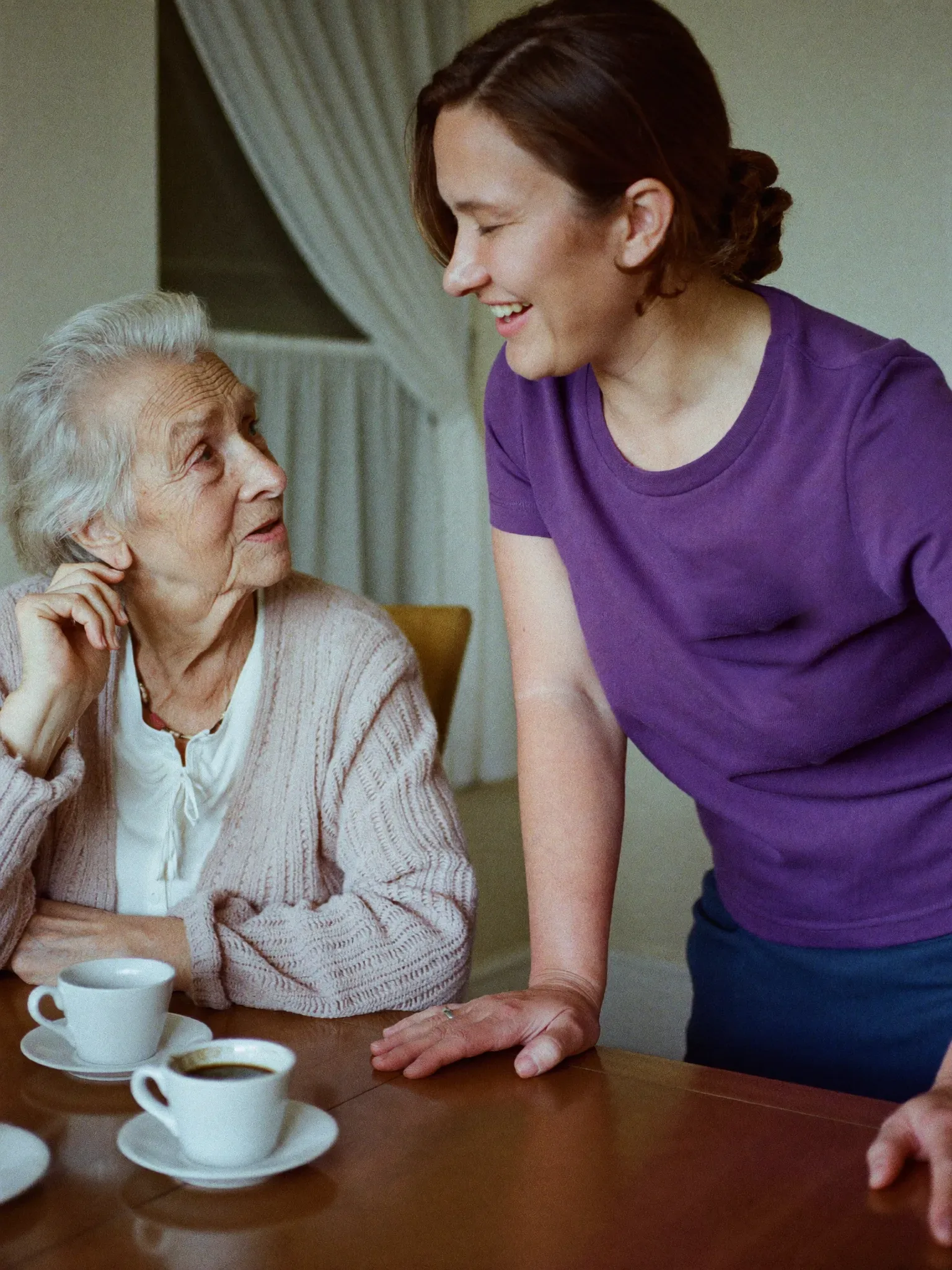 Haushaltshilfe bringt einer Seniorin Kaffee an den Tisch